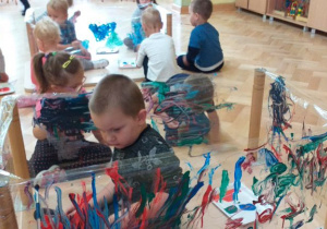 Dzieci malują farbami plakatowymi na folii nawiniętej na nogi stolika.