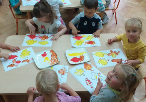 Grupa maluchów maluje palcami zamoczonymi w kolorowych farbach.