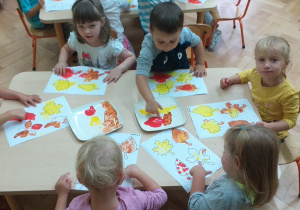 Maluchy malują jesienne liście maczając palce w żóltej, czerwonej i pomarańczowej farbie.