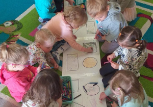 Na długim arkuszu papieru dzieci kolorują obrazek wybranej figury geometrycznej.