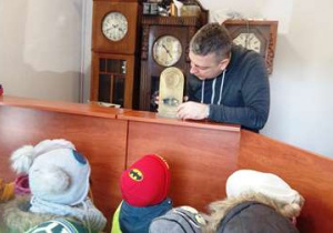 zegarmistrz prezentuje dzieciom dawny zegar stojący.