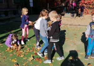 dzieci zbierają liście w ogrodzie przedszkolnym