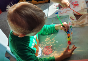Kajtek maluje pisankę farbami.